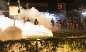 Riot police clear a street with smoke bombs while clashing with demonstrators in Ferguson, Missouri August 13, 2014. Police in Ferguson fired several rounds of tear gas to disperse protesters late on Wednesday, on the fourth night of demonstrations over the fatal shooting last weekend of an unarmed black teenager Michael Brown, 18, by a police officer on Saturday after what police said was a struggle with a gun in a police car. A witness in the case told local media that Brown had raised his arms to police to show that he was unarmed before being killed. REUTERS/Mario Anzuoni (UNITED STATES - Tags: CRIME LAW CIVIL UNREST TPX IMAGES OF THE DAY) - RTR42CPJ